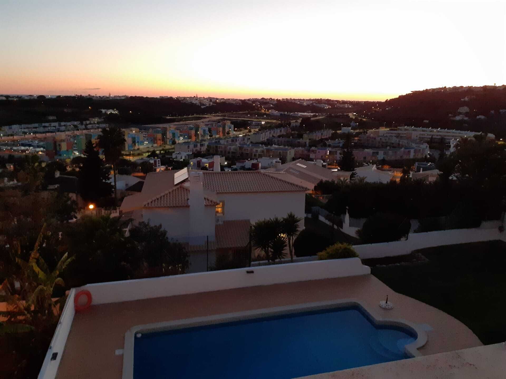 Piscina com vista para uma área residencial ao pôr do sol.