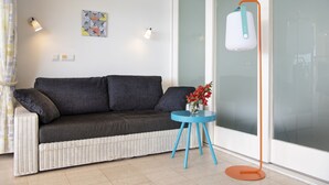 A modern living room with a grey sofa, a blue side table with a vase of flowers, and a floor lamp. - CURACAO OCEAN FRONT APARTMENT WITH PRIVATE DOCK AND A FANTASTIC VIEW (Willemstad)