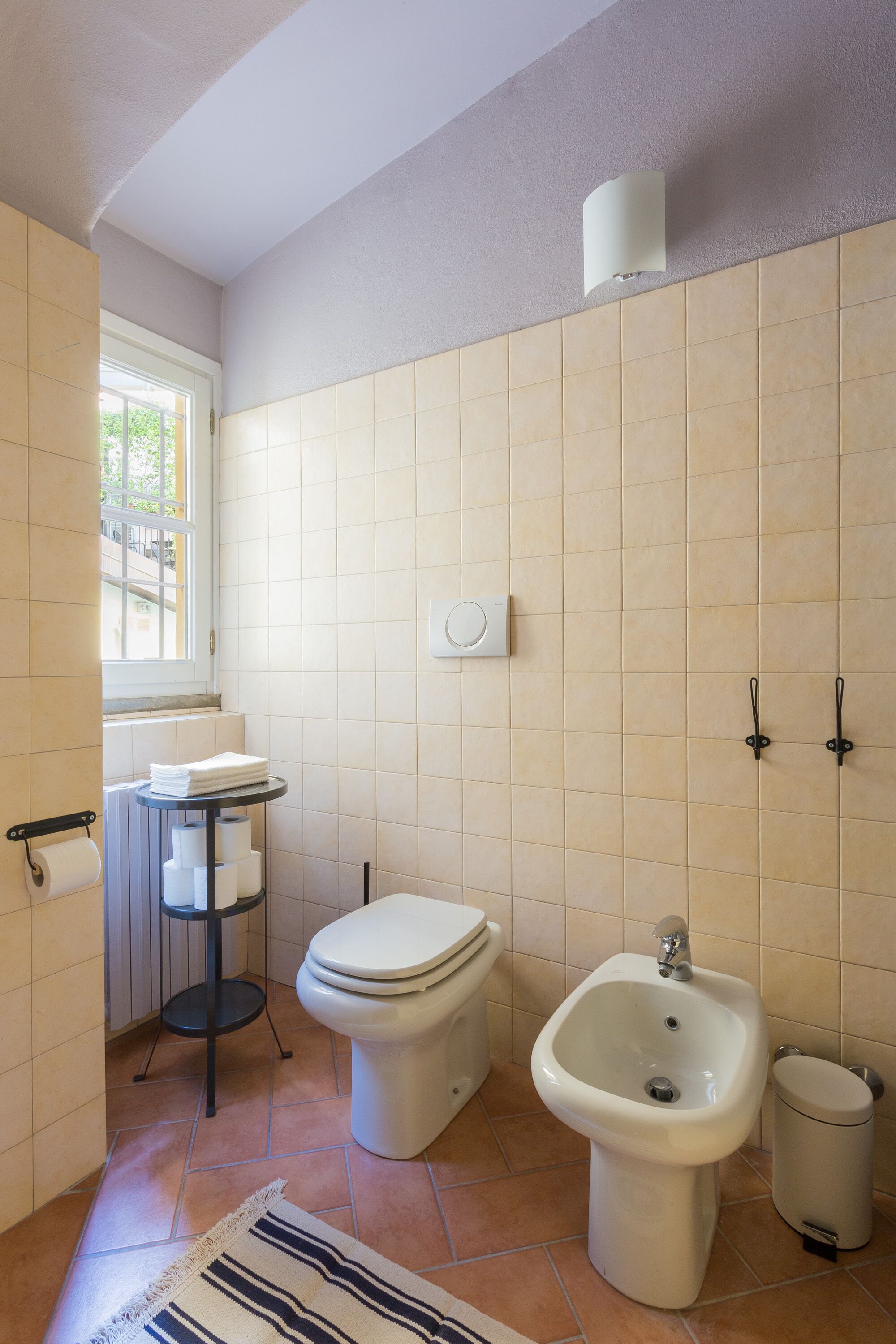 A bathroom with a toilet, bidet, and a small sink with a towel rack.