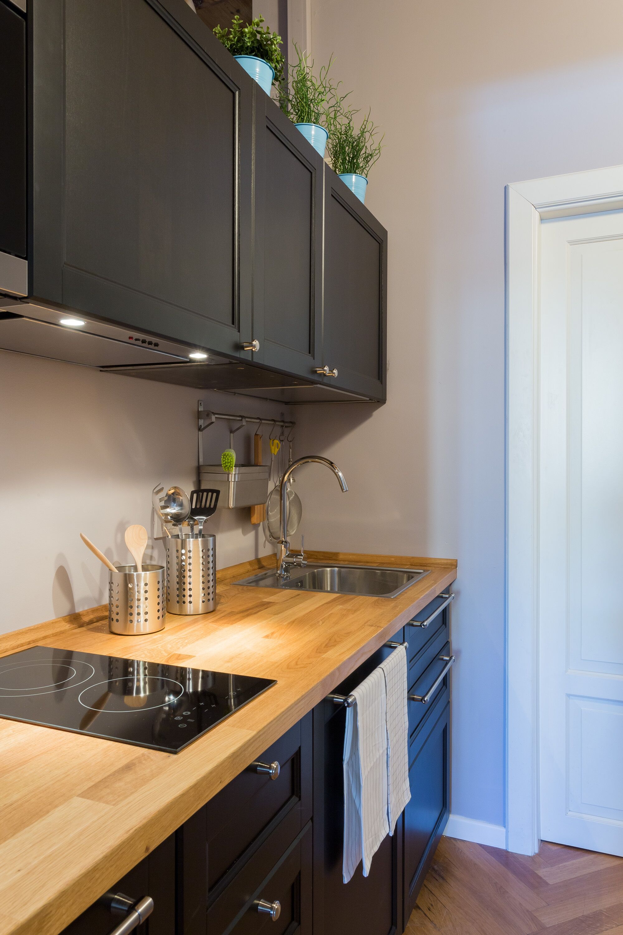 A modern kitchen with a wooden countertop, black cabinets, a built-in oven, and a stainless steel sink.
