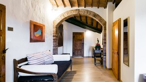 Un pasillo estrecho con un banco de madera a la izquierda, un arco de ladrillo y una puerta de madera al final.