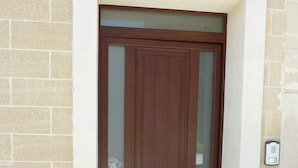 Uma porta de madeira castanha com um painel de vidro, emoldurada por uma estrutura branca, com um fundo de parede de tijolos.