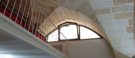 A stone-walled interior with a white staircase leading to a balcony.