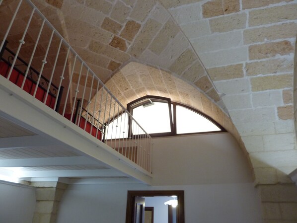 Ein Innenraum mit Steinwänden und einer weißen Treppe, die zu einem Balkon führt.