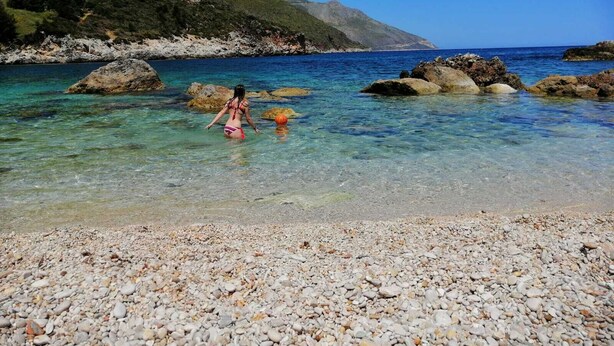 A pebbled beach with clear water and rocky outcrops.