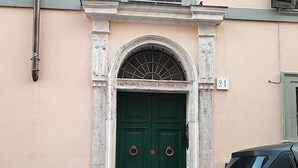 Una puerta verde con un tirador de metal en forma de anillo, un letrero con el número '21' encima, y un vehículo estacionado a la derecha.