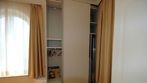 Un armario con espacio para colgar y estantes, una caja de detergente para la ropa, y una puerta que da a otra habitación.