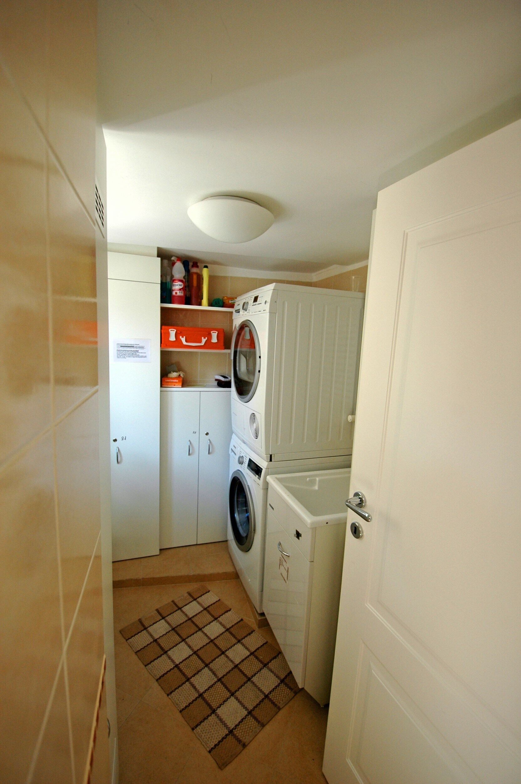Une petite buanderie équipée d’un lave-linge, d’un sèche-linge et de placards de rangement.
