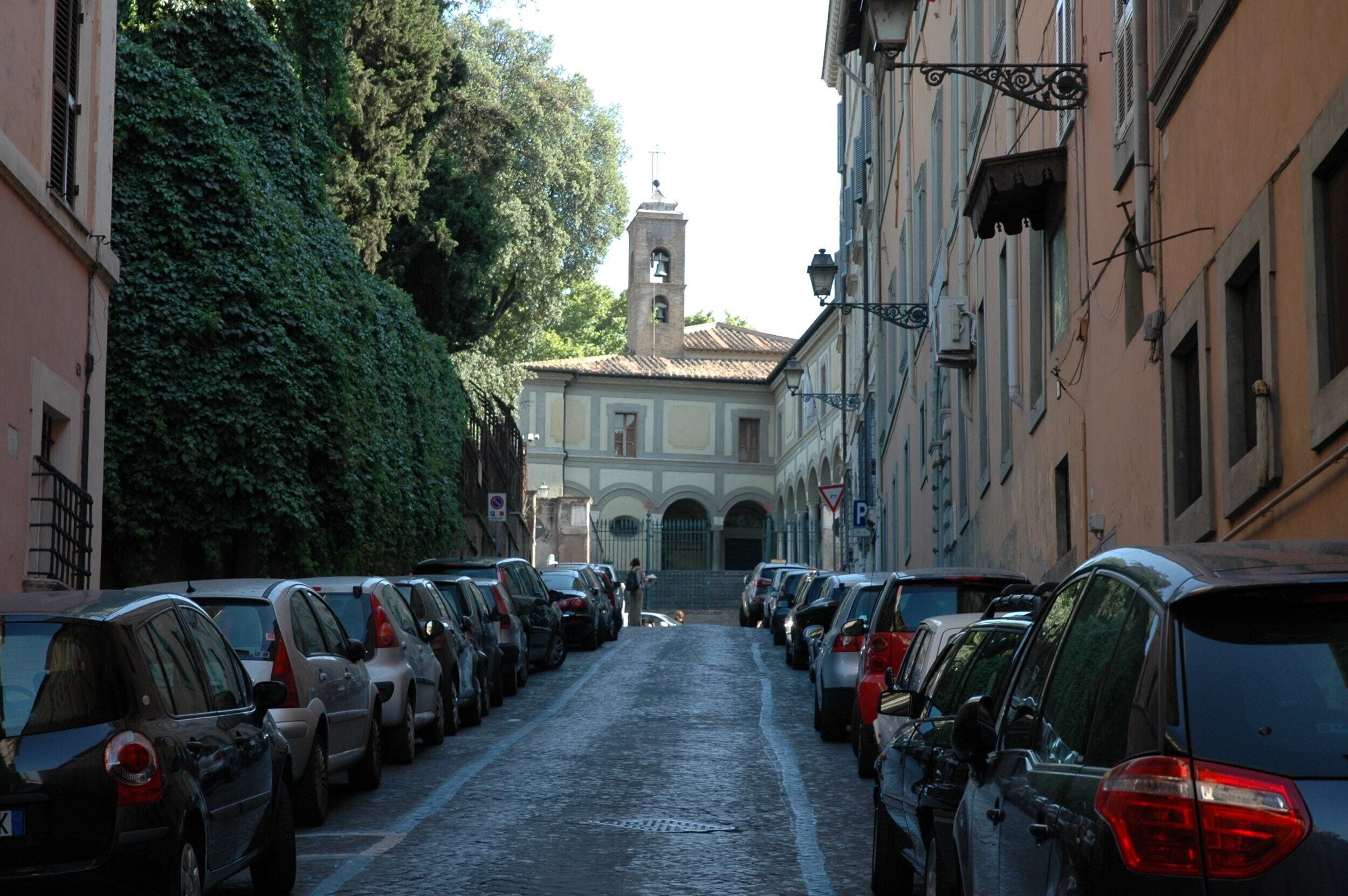 A narrow cobblestone street lined with parked cars and buildings on both sides.