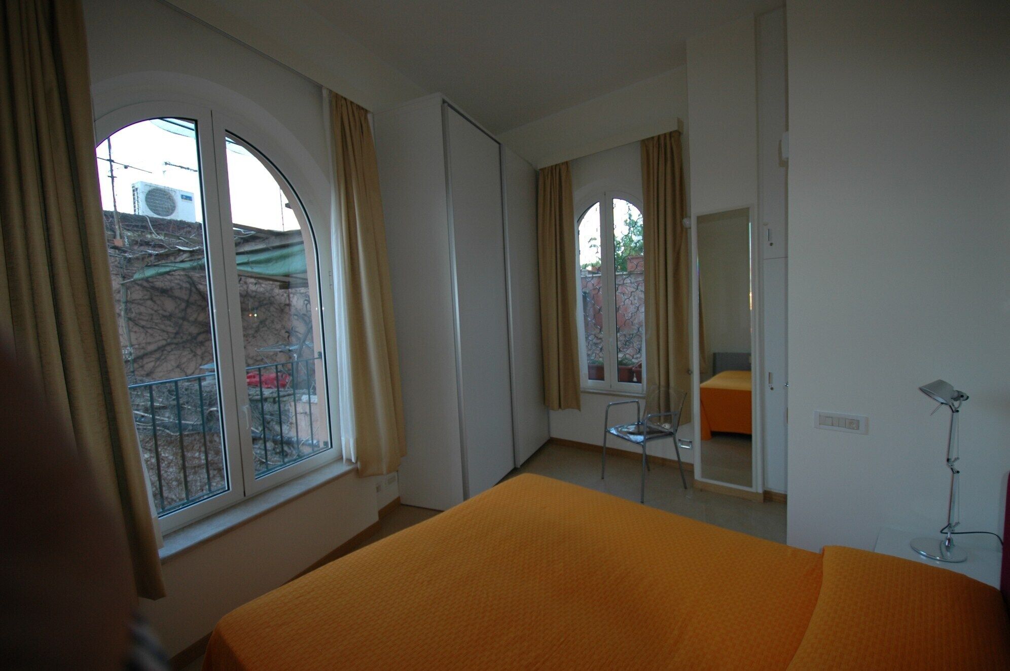 Une chambre avec une grande fenêtre, un lit, une chaise, un miroir et une lampe de bureau.