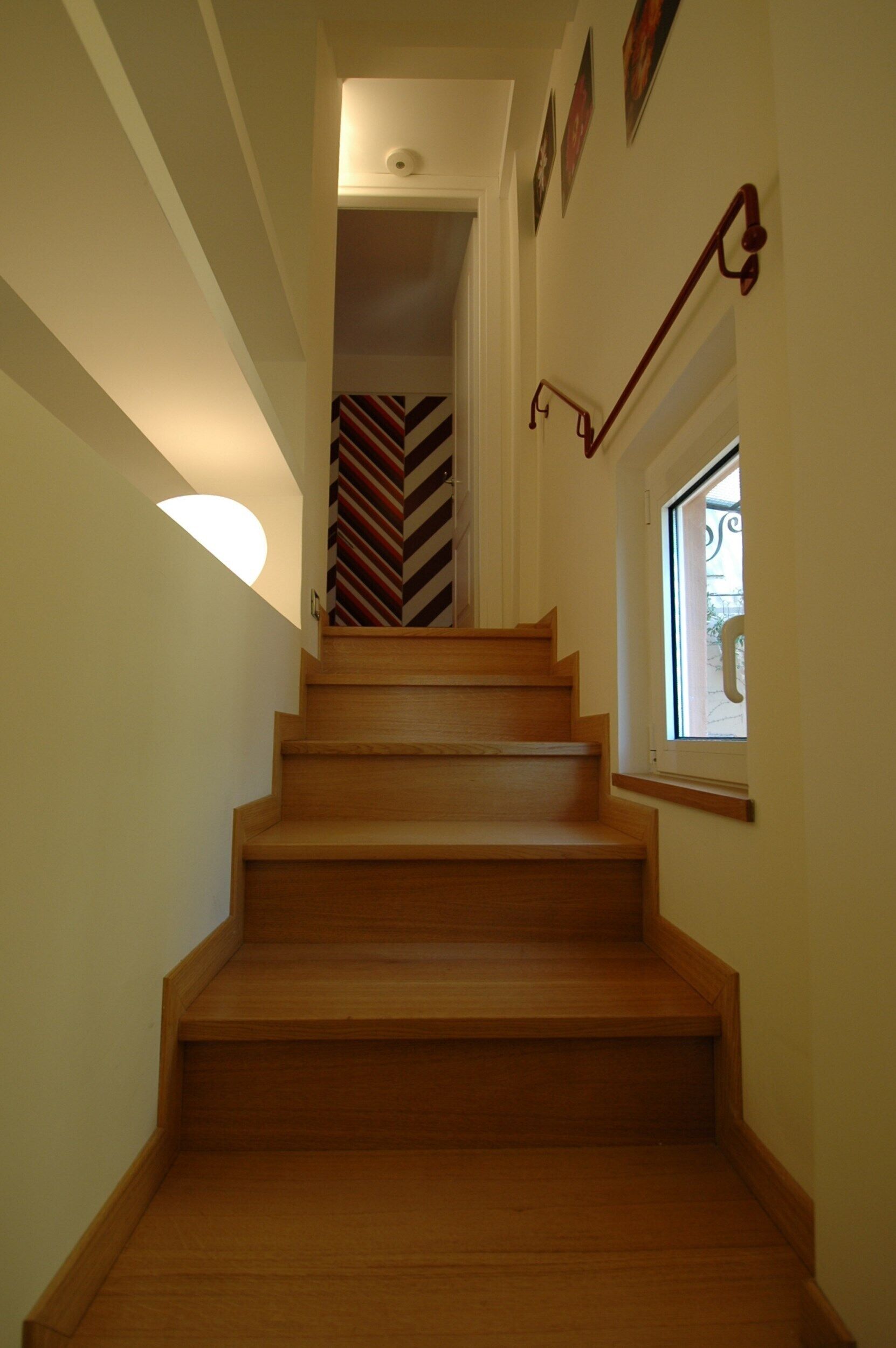 A wooden staircase with a handrail, a light fixture on the left, and a window on the right.