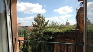 Un balcón con vista a un paisaje urbano, que incluye un edificio con forma de cúpula y cielo despejado.