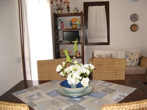 Une table à manger agrémentée d’un centre de table floral, un téléviseur posé sur une étagère et un canapé à l’arrière-plan.