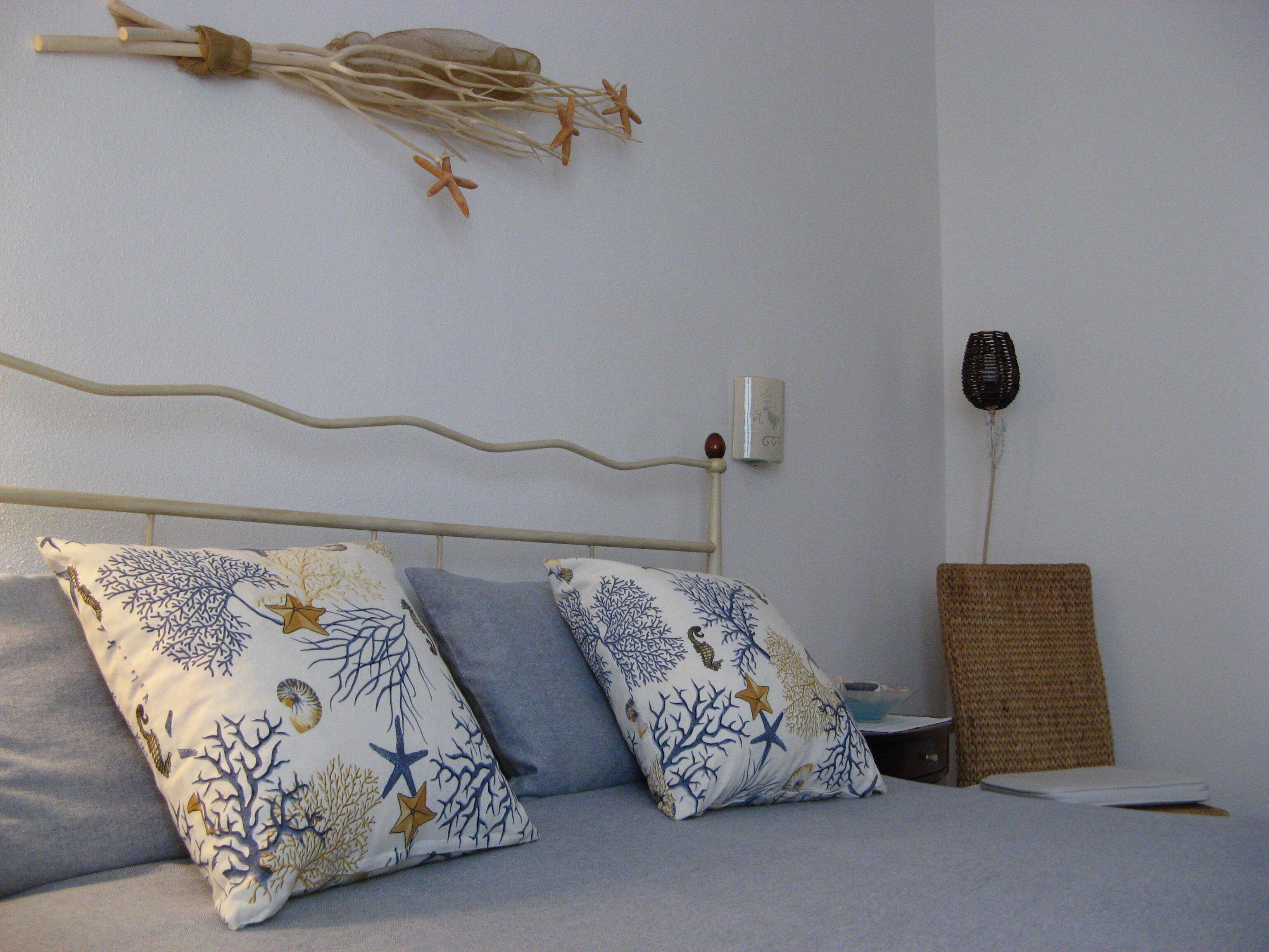 A bed with two pillows, a bedside table, a wall-mounted lamp, and a woven basket.