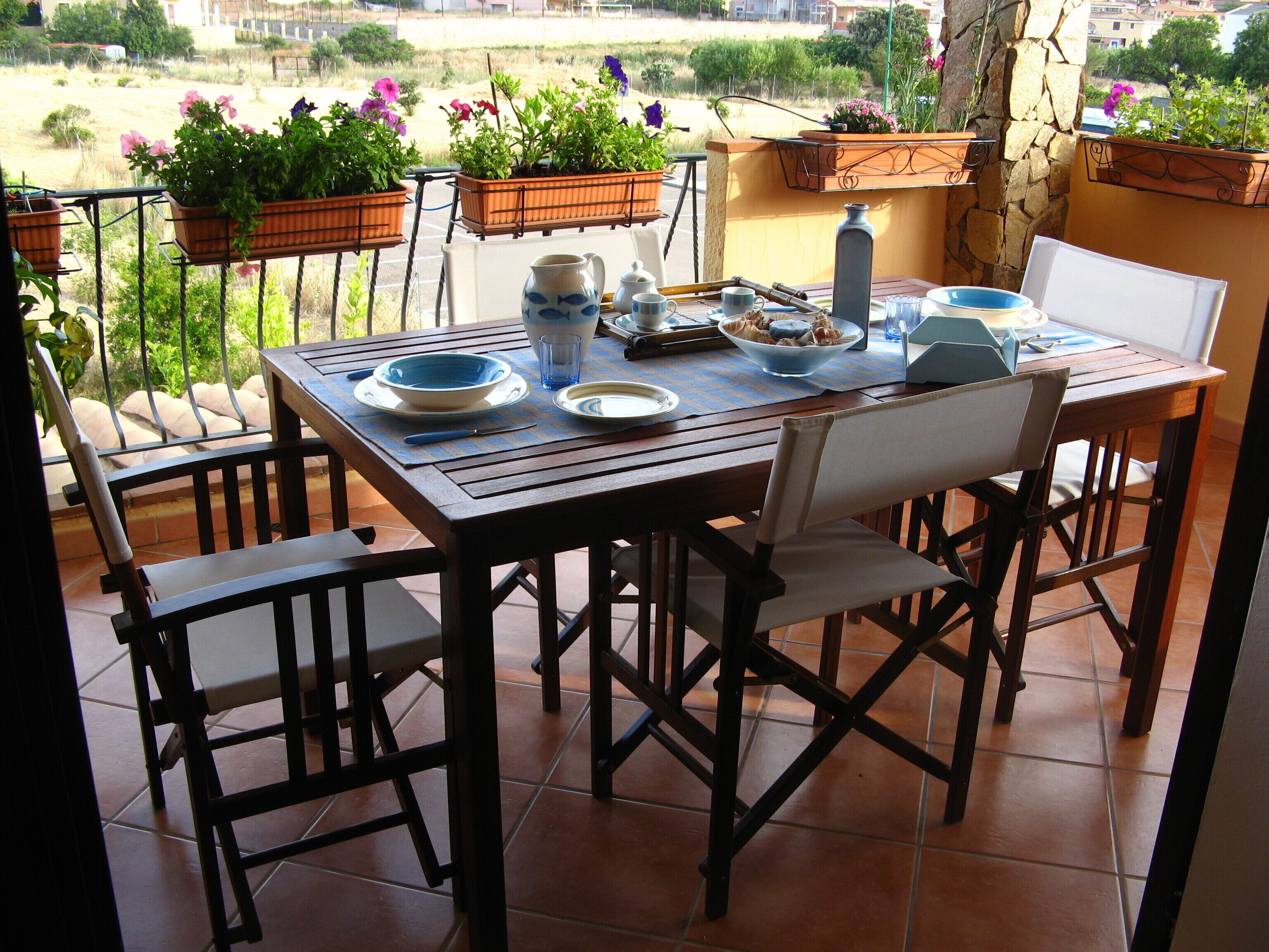 A patio table set with plates, bowls, and a pitcher, surrounded by chairs.