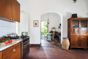 A kitchen with a stove, oven, and wooden cabinets. There is a dining area with a table and chairs, and a wicker basket on the floor.