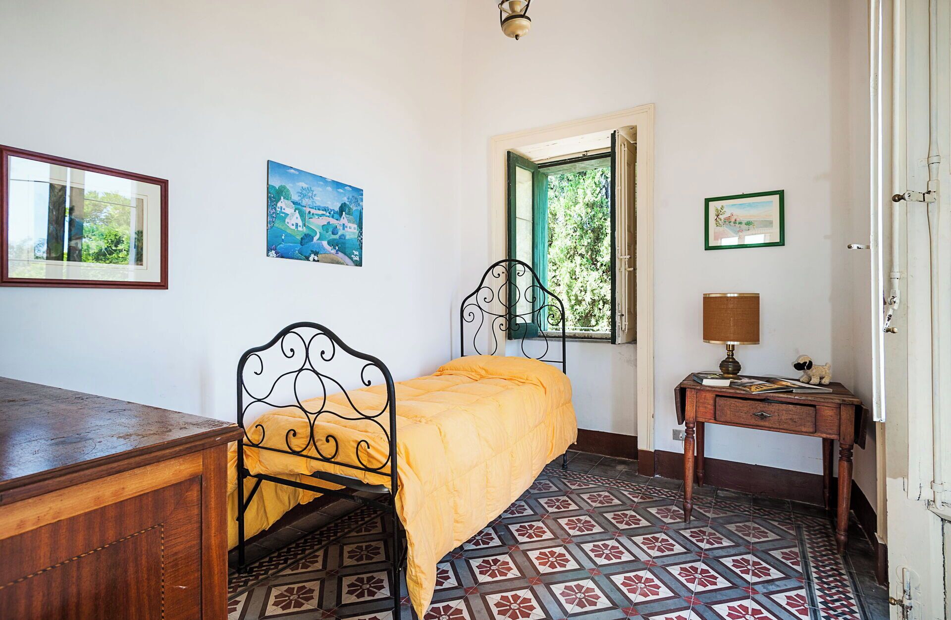Un dormitorio con una cama individual, un escritorio de madera, una lámpara y una ventana con vista a zonas verdes.