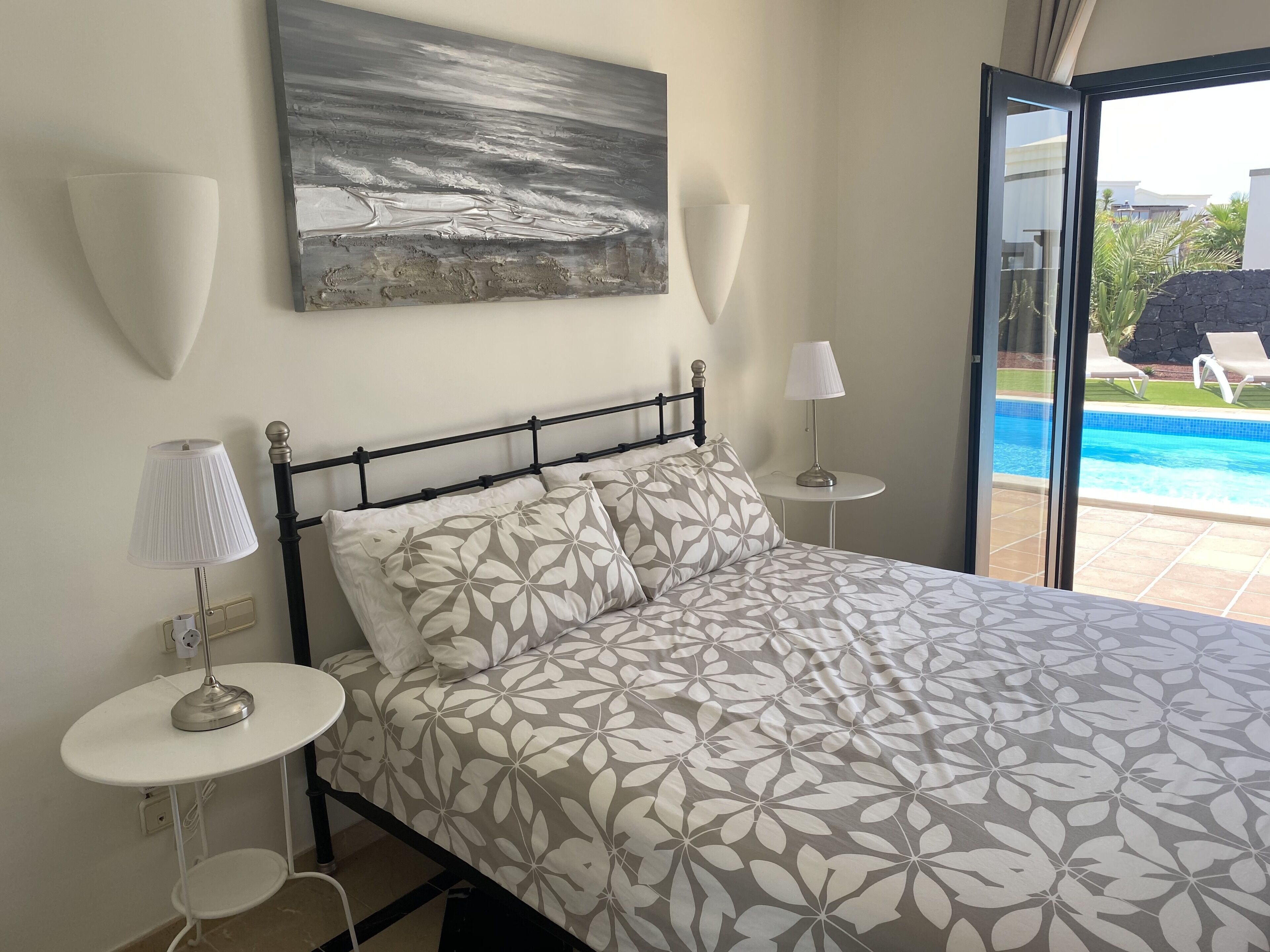 Een slaapkamer met een bed, twee nachtkastjes, een wandlamp en een schilderij.