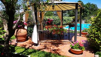 Un’area salotto all'aperto riparata, con vasi in terracotta e una piscina sullo sfondo.