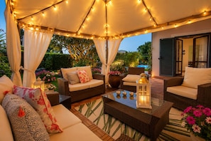 An outdoor seating area with wicker furniture, a glass coffee table, and string lights. - House / Villa - Rignano Flaminio (Rignano Flaminio)
