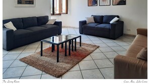 Ein Wohnzimmer mit zwei dunklen Sofas, einem Glastisch und einem braunen Teppich. An der Wand hängen drei gerahmte Kunstwerke.