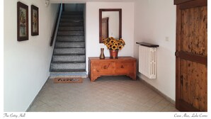 Ein Korridor mit einer Holztreppe, einem Konsolentisch aus Holz mit einer Vase Sonnenblumen, einem Heizkörper und einer großen Holztür.