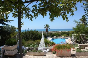 Zona de piscina con vistas al mar, rodeada de vegetación y plantas en macetas.