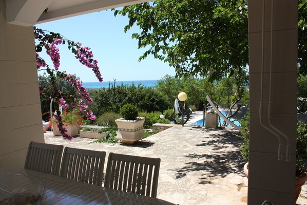 Un patio con vistas al mar, mobiliario exterior y plantas en macetas.