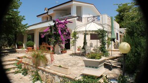 Une maison à deux étages dotée d’un patio couvert, de meubles d’extérieur et de plantes en pot.