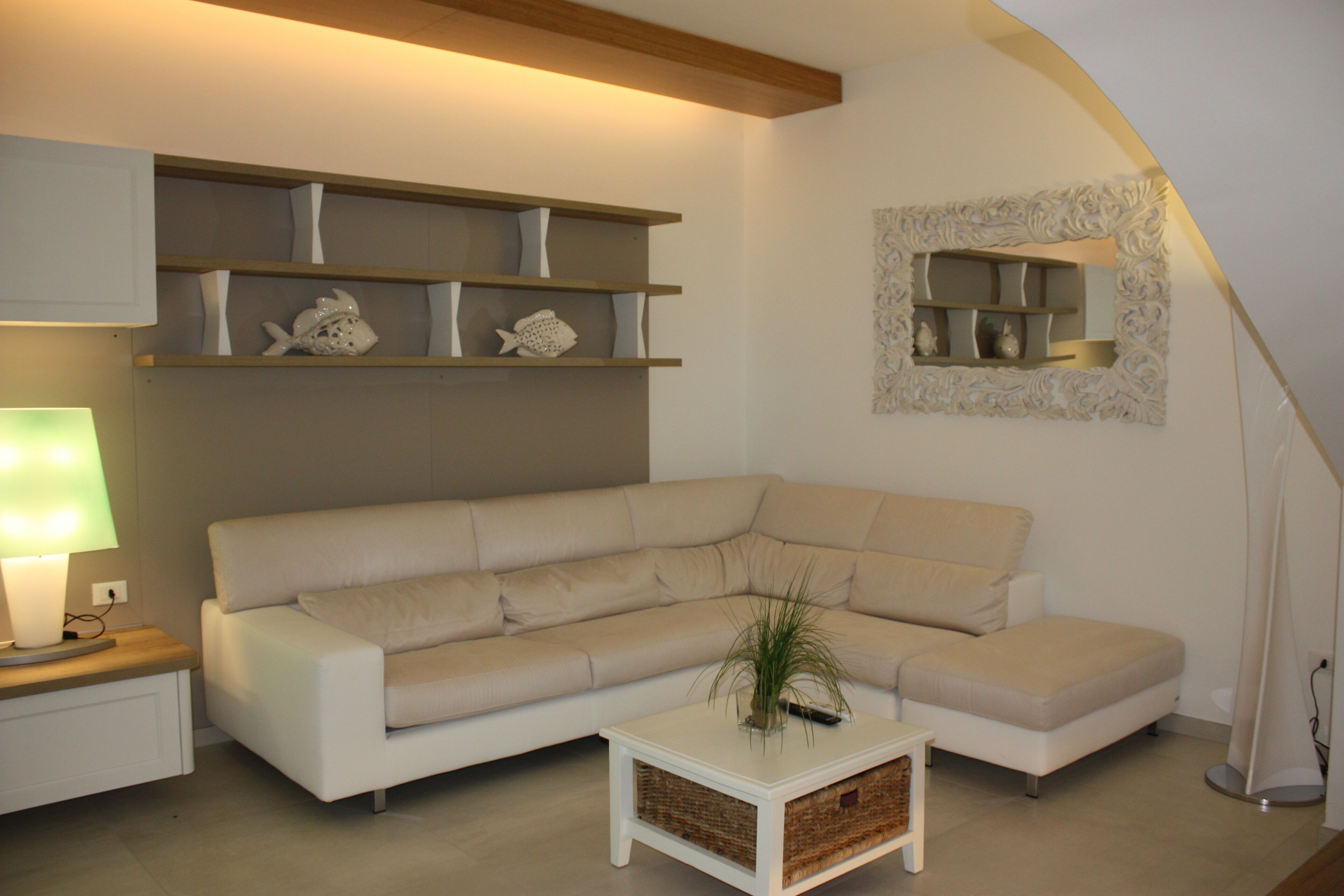 A modern living room with a beige sectional sofa, a white coffee table, and a decorative mirror on the wall.