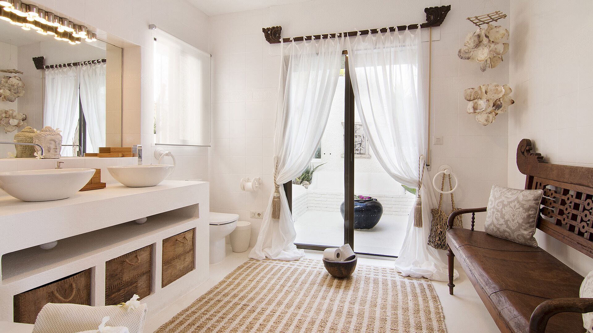 Une salle de bain avec un grand miroir, deux lavabos, des toilettes et un banc.