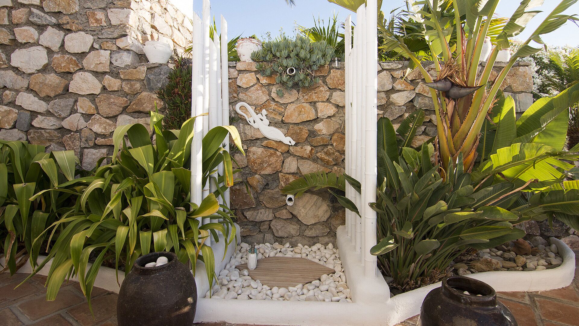 A garden with various plants, a stone wall, and a white fence.