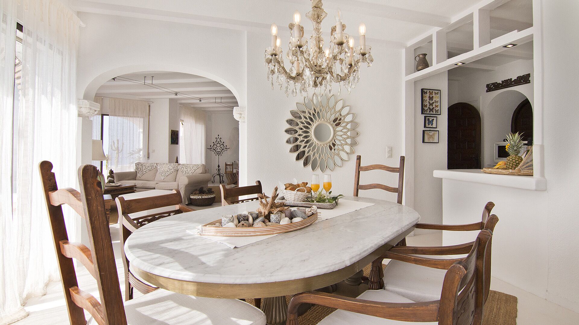A dining area with a round marble table, wooden chairs, a chandelier, and a decorative mirror.