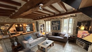 A cozy living room with a fireplace, a dining area, and a kitchen. - Charming house, enclosed garden, 3 min from Arromanches and the beaches (Ryes)