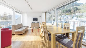 Een ruime kamer met een grote eettafel, houten stoelen, een bank en een televisie.