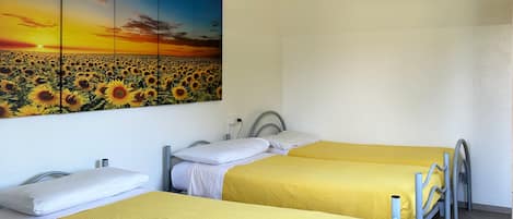 Una habitación con dos camas, cada una con cubrecama amarillo, un cuadro grande de un campo de girasoles y una pared blanca.