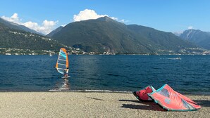 A lake with a windsurfing board and two kites on the shore.