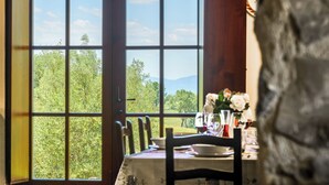 A dining table with chairs, set for a meal, and a view of a green landscape through large windows. - Montebendico 6, Emma Villas (Montegiovi - Castel del Piano (Grosseto))