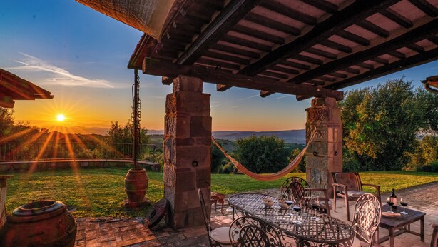 A patio with a table and chairs, a hammock, and a view of the sunset over a landscape. - Montebendico 6, Emma Villas (Montegiovi - Castel del Piano (Grosseto))
