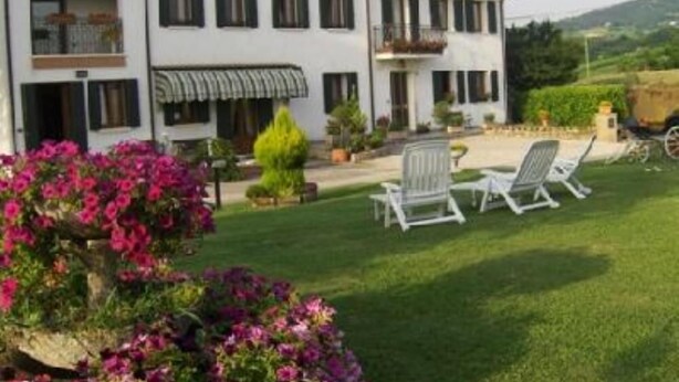 A two-story building with a white facade and a tiled roof. There are two balconies with black railings, and a covered patio area with outdoor furniture. - By: An hour from VENICE, in the park of the Colli Euganei - Tourist Locations (Vò)