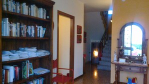 A room with a large wooden bookshelf filled with books, a red folding chair, a fireplace, and a staircase leading to another level. - By: An hour from VENICE, in the park of the Colli Euganei - Tourist Locations (Vò)