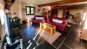 A spacious living room with dark tiled flooring, two red leather sofas, a wooden coffee table, and a television.