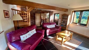 A spacious living room with two red leather sofas, a wooden coffee table, and a staircase leading to an upper level.