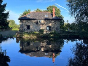Ein Haus aus Stein mit rotem Dach, das sich in ruhigem Wasser spiegelt.