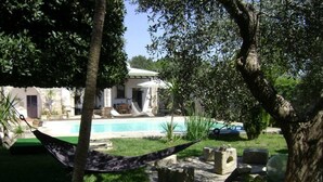 Una hamaca en un jardín exuberante con piscina y un muro de piedra.