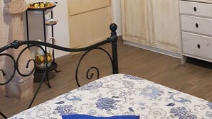 Una habitación con techo inclinado, una cama con colcha estampada, un aparador de madera, una mesita con una taza y una puerta con paneles de vidrio esmerilado.