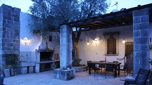 Un patio al aire libre con paredes de piedra, una pérgola de madera, una chimenea de piedra y una mesa con sillas.