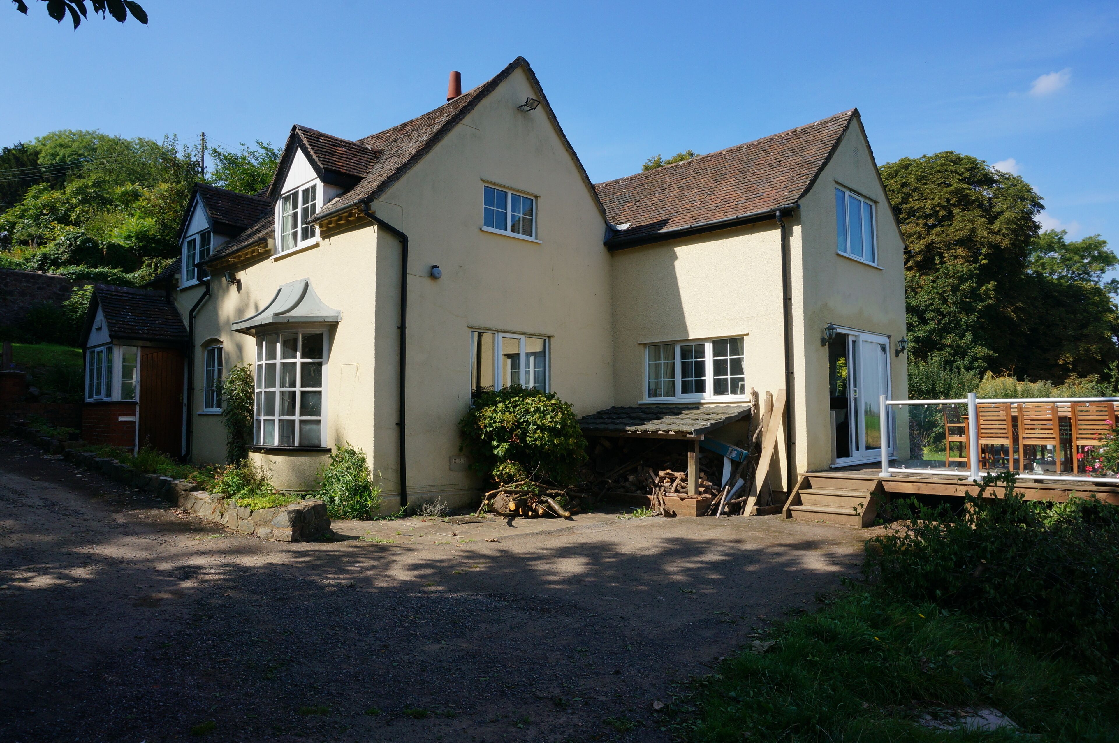 A two-story house with a sloped roof, a front porch, and a small garden area.