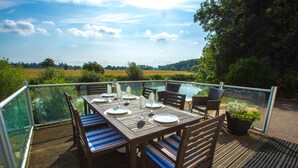 A dining table set outdoors with chairs, a glass railing, and a view of a field and trees. - Historic detached cottage, on the banks of the River Severn Nr Upton & Malvern (Worcestershire)