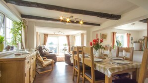 A dining area with wooden chairs and a table set for four, a wooden cabinet, and a plant on the windowsill. - Historic detached cottage, on the banks of the River Severn Nr Upton & Malvern (Worcestershire)
